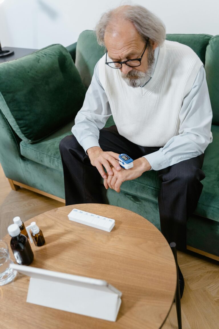 Elderly man sitting on couch checking pulse with oximeter indoors.